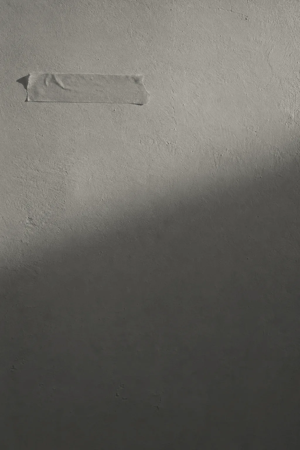 A pale plaster wall in raking light, a strip of tape on it: Spine's kept picture moment-2, in Spine's black and cream under a dot screen.